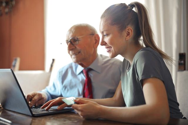 a girl holding a creditcard infront of a laptop with an elderly